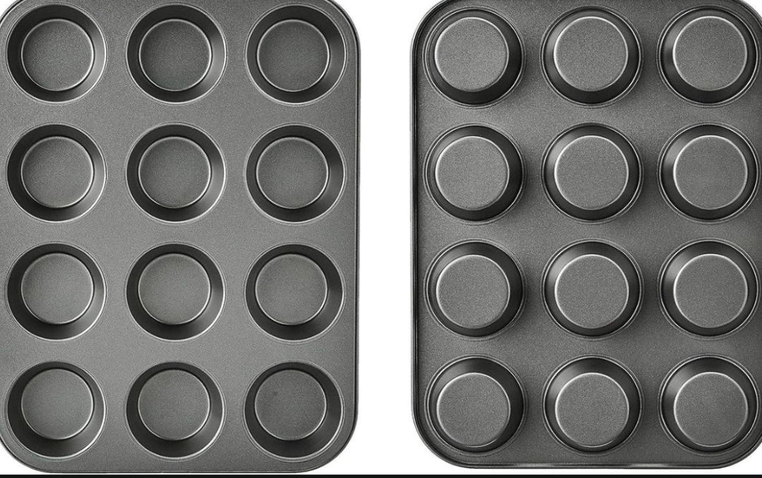 Two dark gray non-stick 12-cup muffin pans shown side by side against a white background, with a large black block obscuring the lower half of the image.