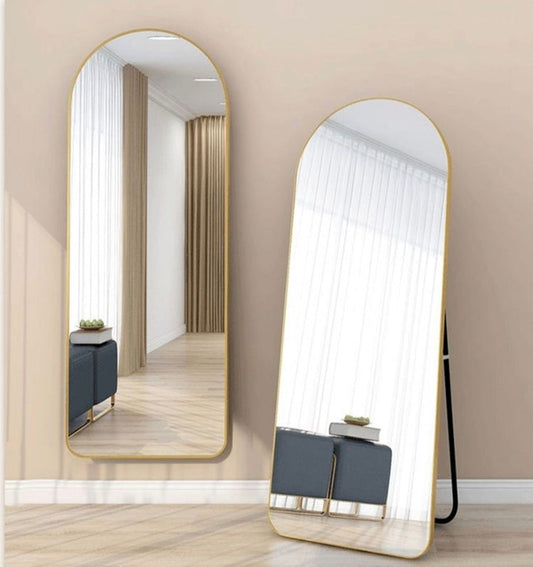 Two arched full-length floor mirrors with gold frames, shown leaning against a beige wall in a modern room setting.