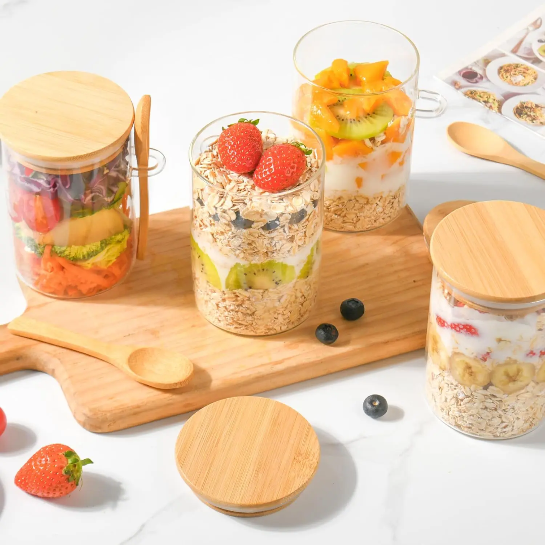 Glass jars with wooden lids containing layered breakfast foods on a white surface.