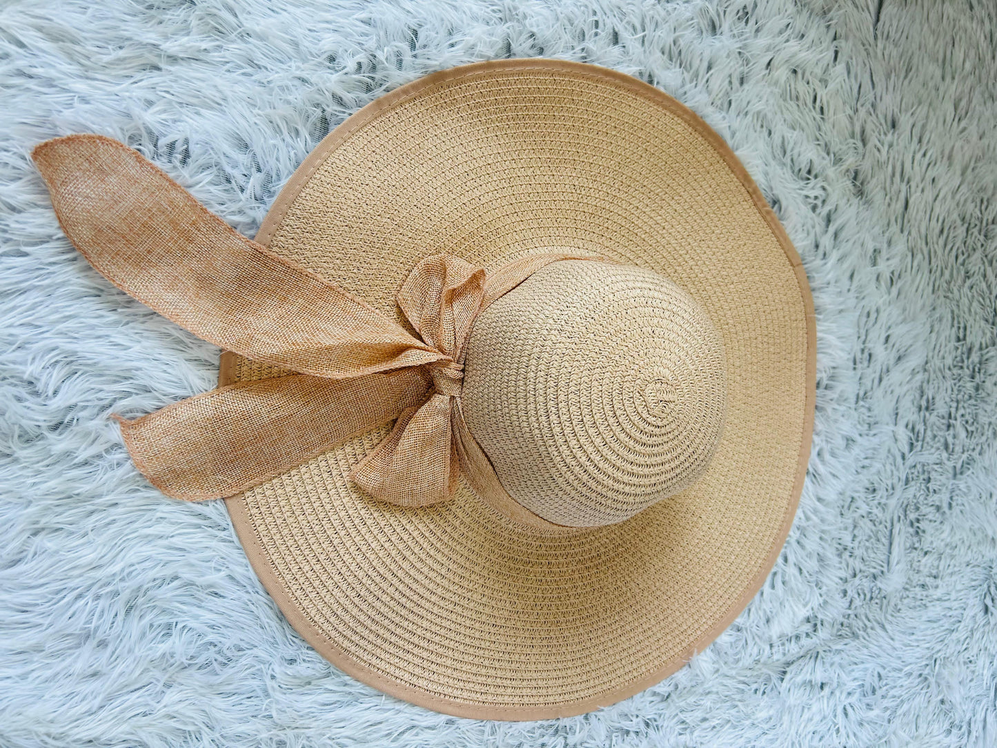 Beige straw hat with a bow on a fluffy white surface