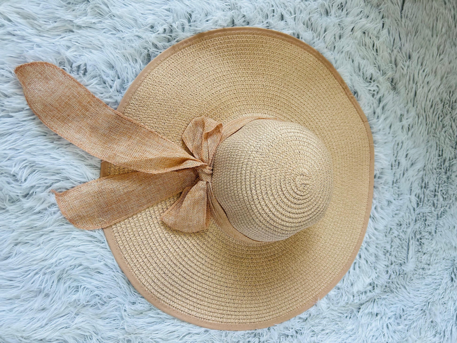 Beige straw hat with a bow on a fluffy white surface