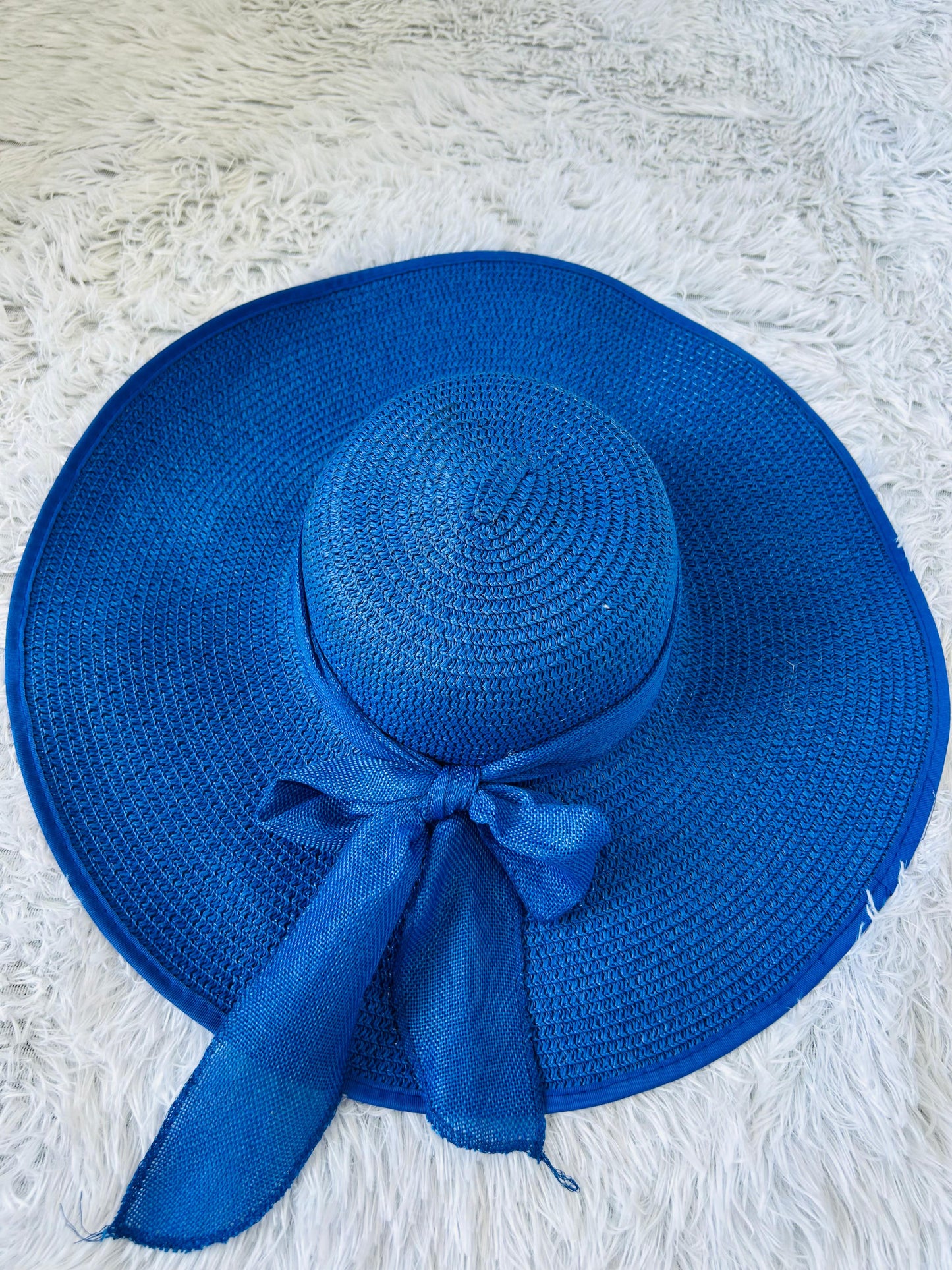 Blue straw hat with a ribbon on a textured white surface