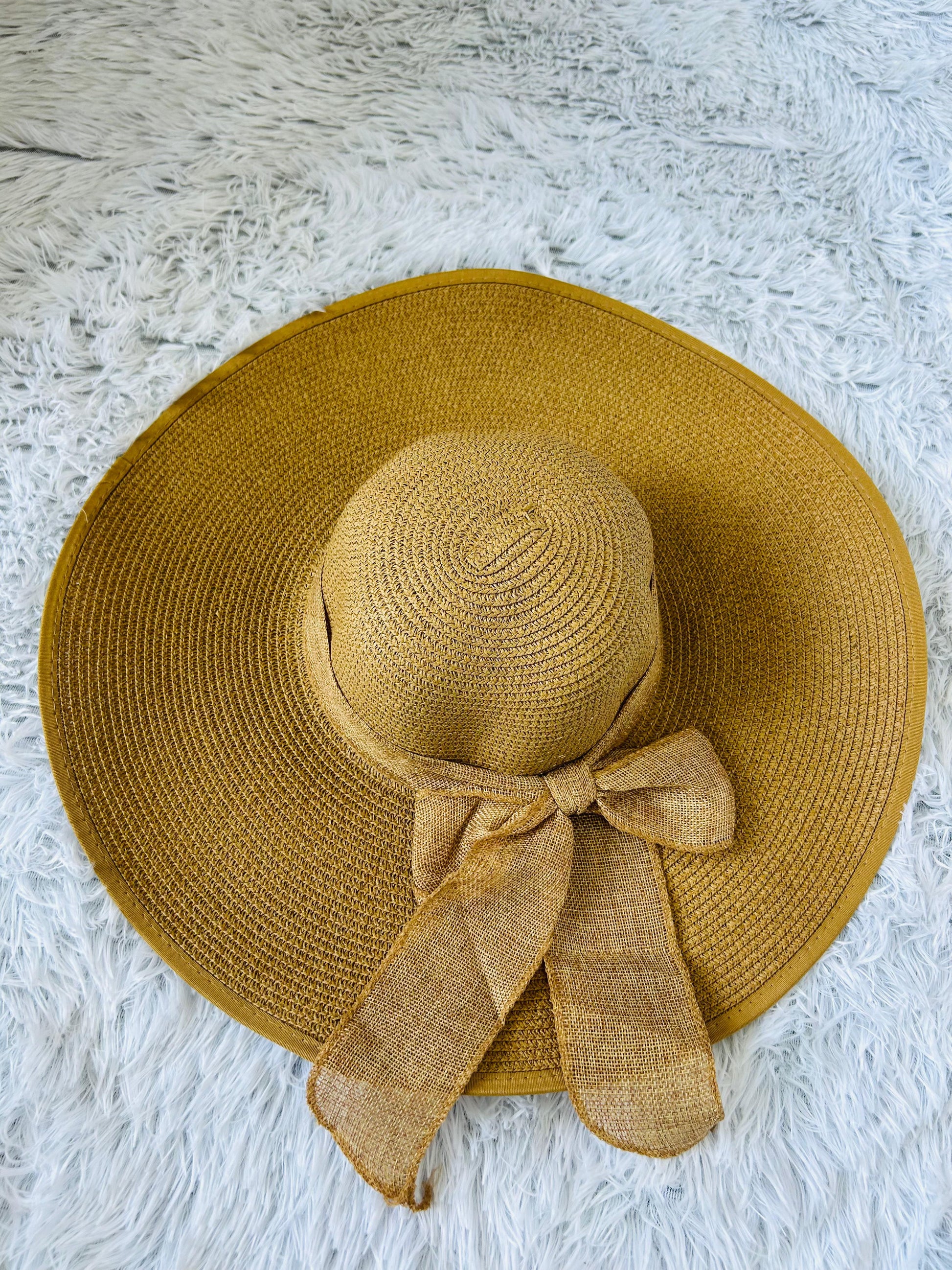Khaki straw hat with a bow on a white textured surface