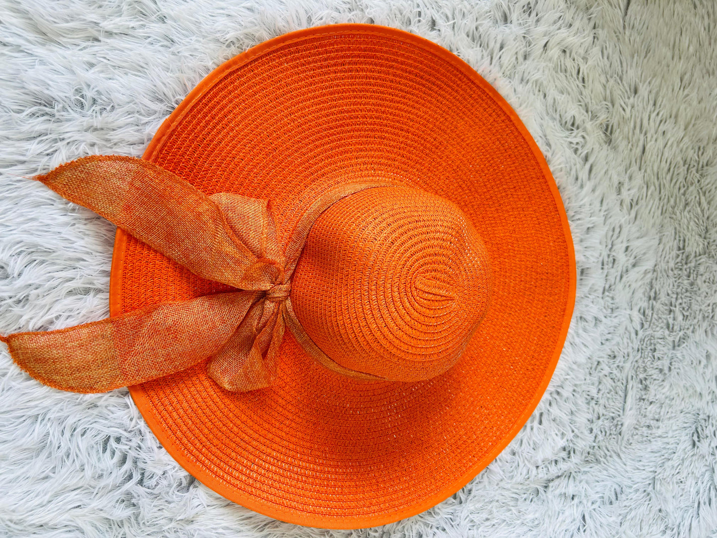 Orange straw hat with a ribbon on a white fluffy surface