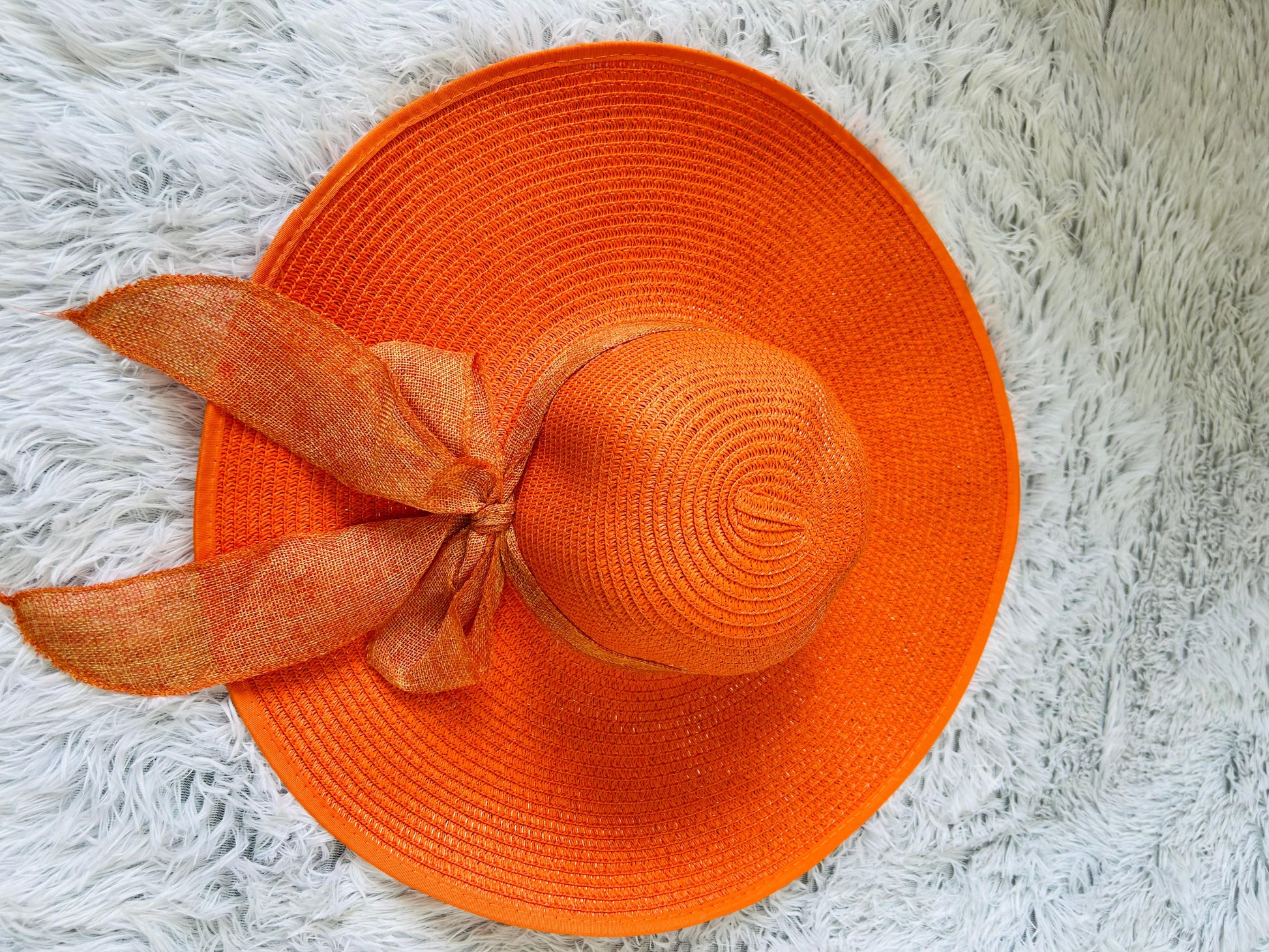 Orange straw hat with a ribbon on a white fluffy surface