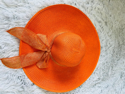 Orange straw hat with a ribbon on a white fluffy surface