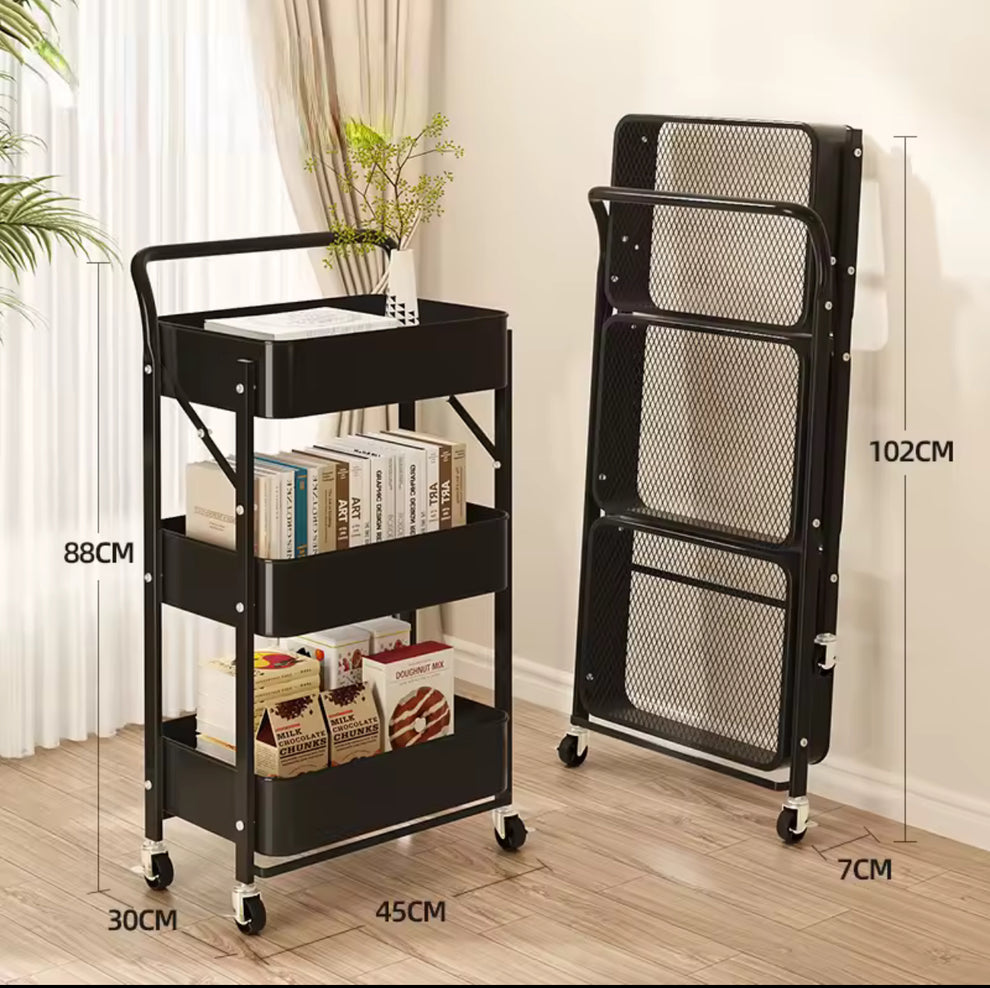 Black metal rolling storage cart shown in both open and folded positions, with dimension labels indicating 102CM height, 7CM wheel width, 30CM depth, and 45CM width. The cart is placed on a wood floor against a light wall, with books and a plant as props.