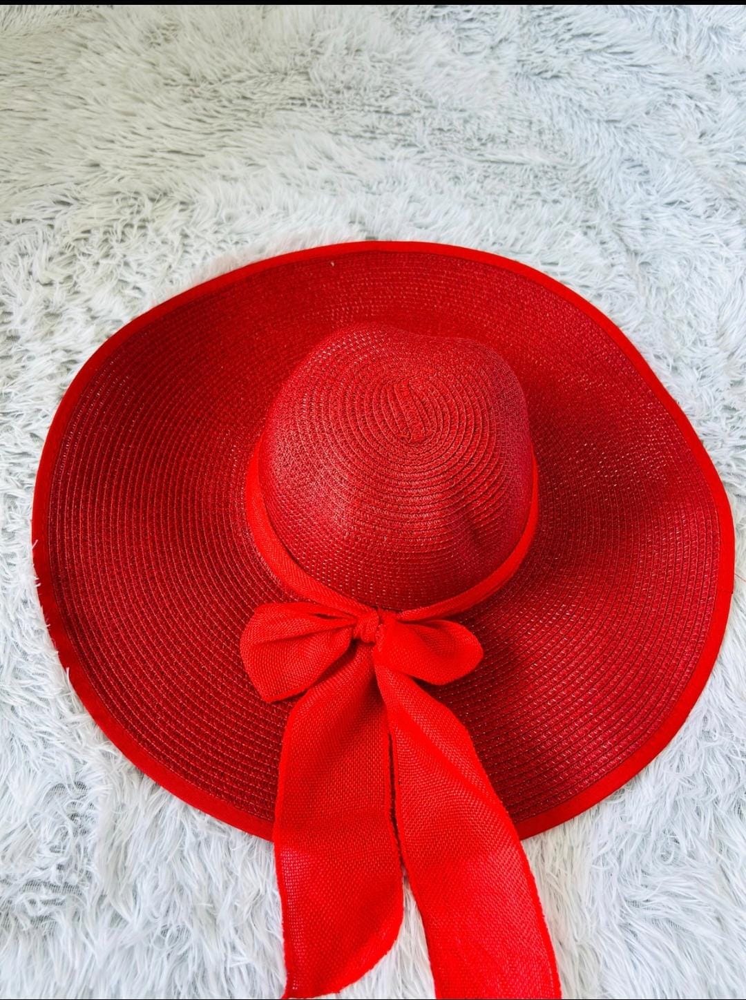 Red straw hat with a bow on a white textured surface