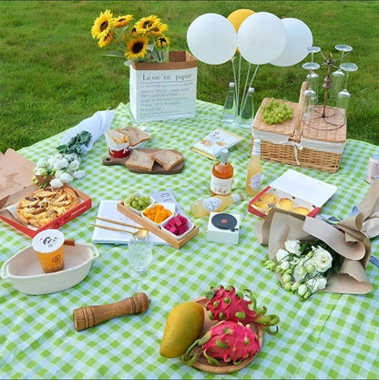 Picnic setup with food, drinks, and decorations on a green checkered blanket.