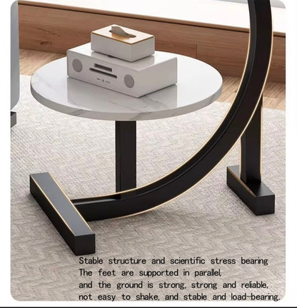 Round side table with marble top and black curved legs on a wooden floor.