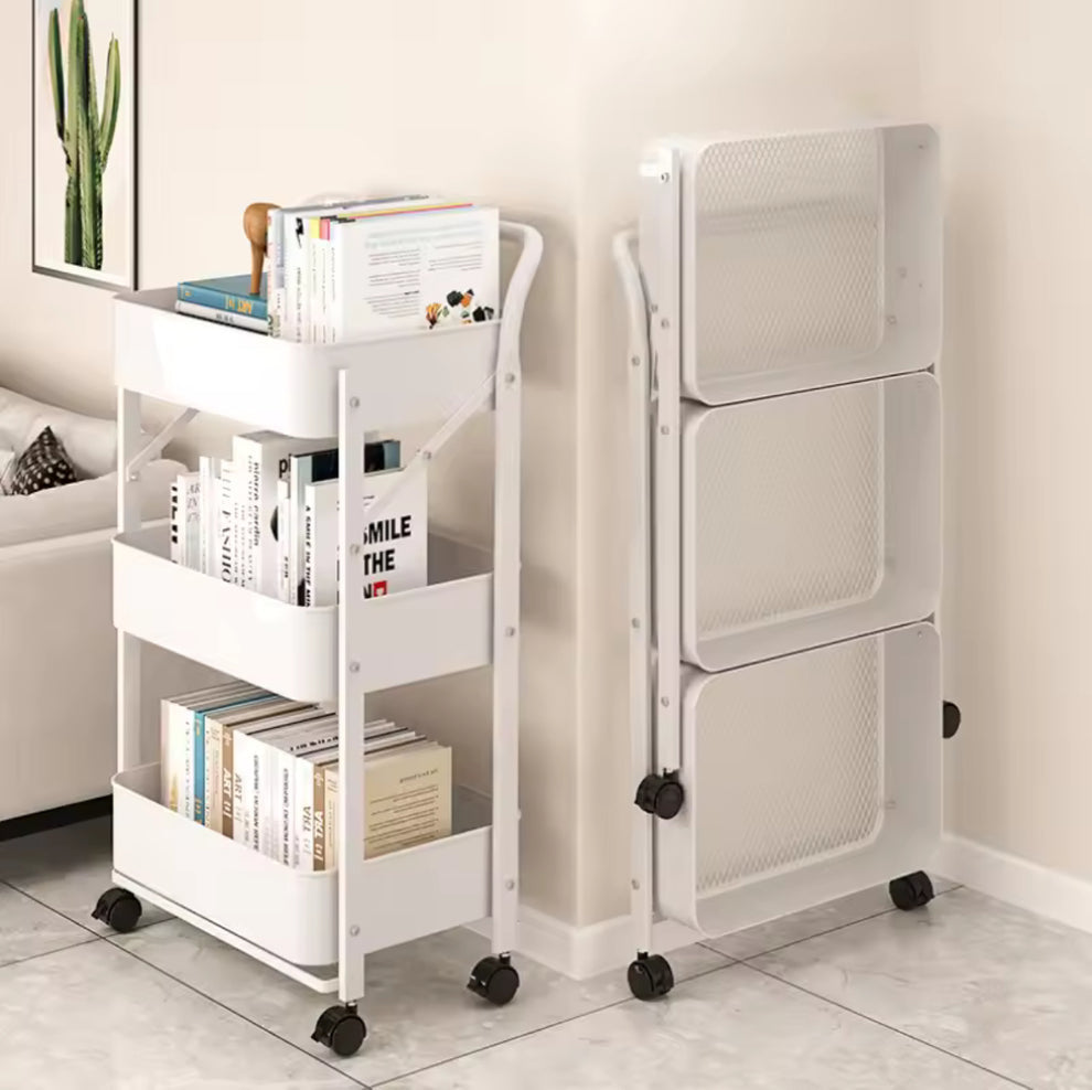 A white three-tier rolling bookshelf shown in two positions: one fully loaded with books and magazines, and one empty, folded flat to show its compact storage design. The bookshelf is set in a minimalist room with beige walls and light gray tiled flooring.