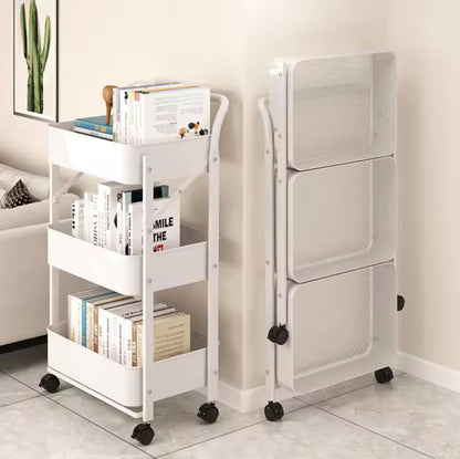 A white three-tier rolling bookshelf shown in two positions: one fully loaded with books and magazines, and one empty, folded flat to show its compact storage design. The bookshelf is set in a minimalist room with beige walls and light gray tiled flooring.