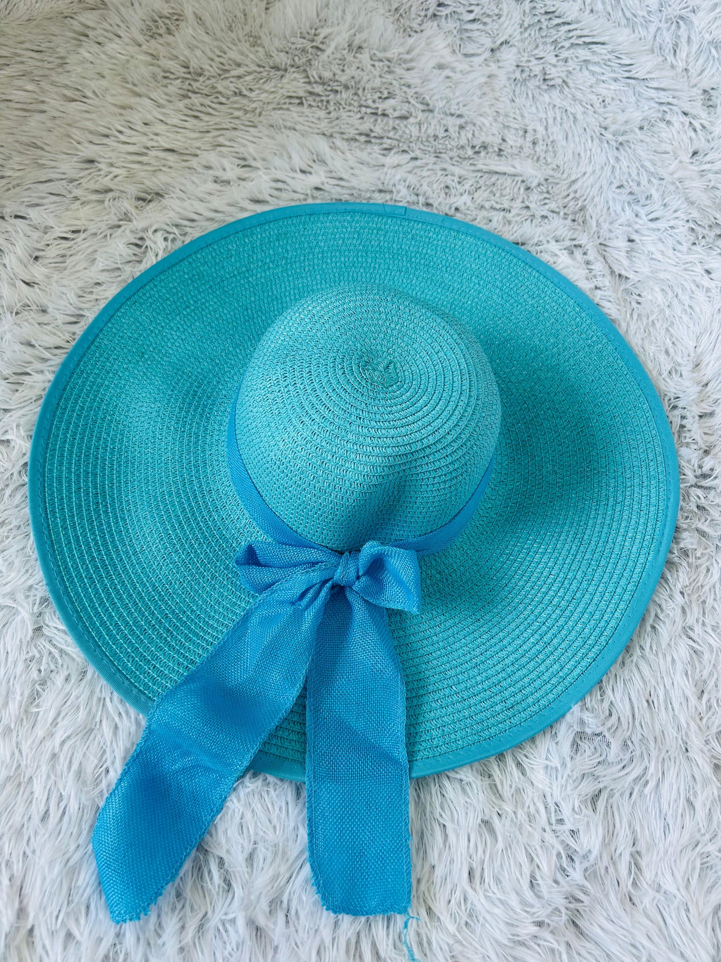 Turquoise straw hat with a matching ribbon on a textured white surface