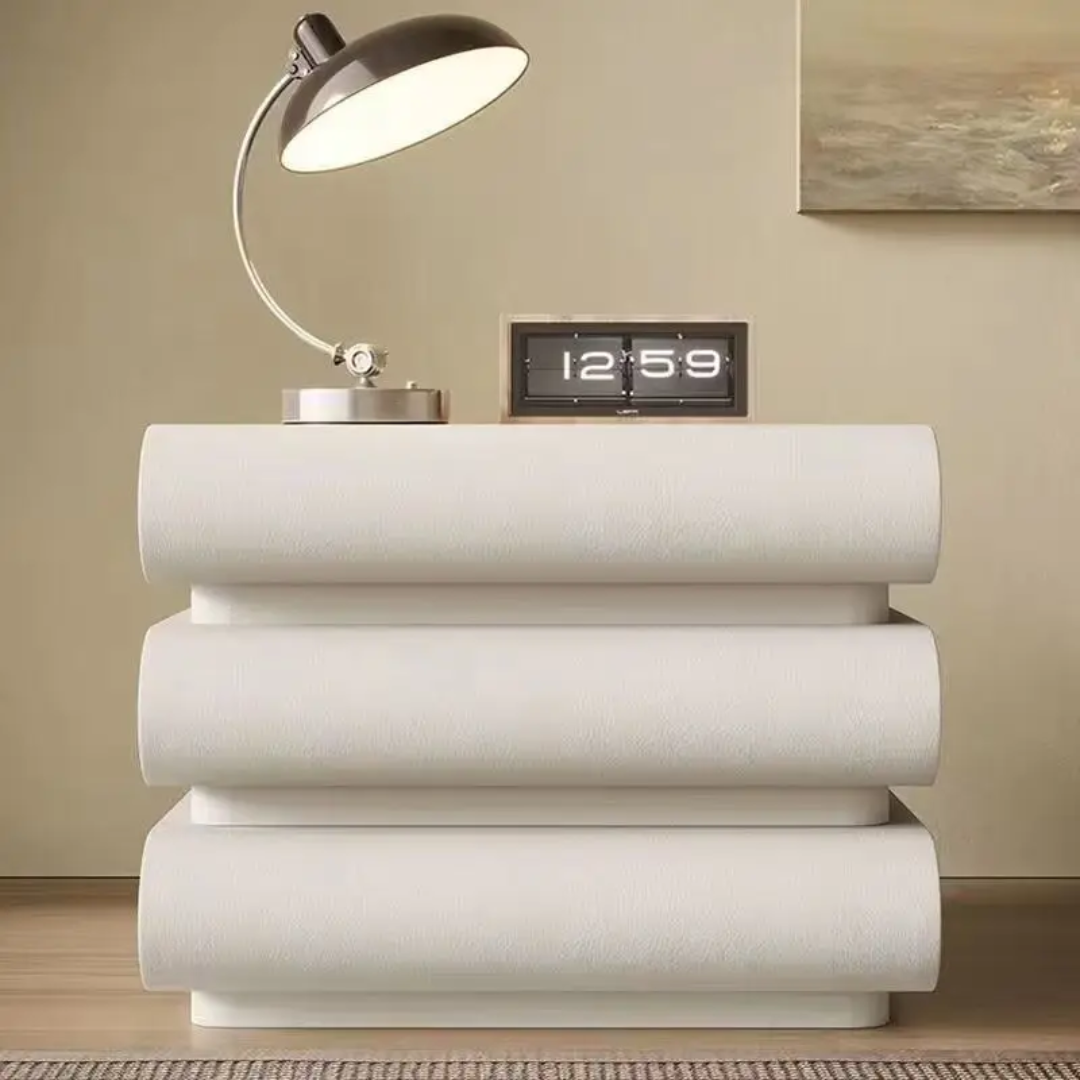 White decorative table with a lamp and digital clock on top against a beige wall.