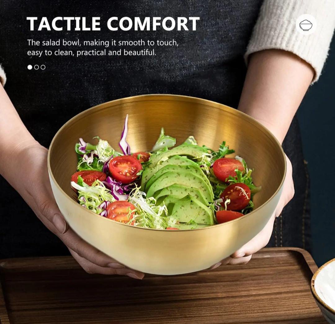 Person holding a gold salad bowl filled with a colorful salad on a wooden surface.