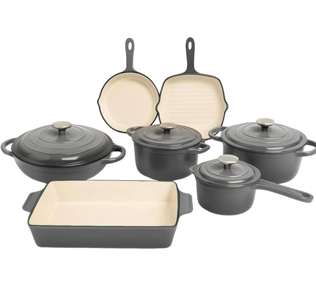 A 7-piece cast iron cookware set in dark gray with cream-colored interiors, including a rectangular baking dish, two saucepans, a pot with lid, a skillet, and a griddle plate, arranged on a white background.