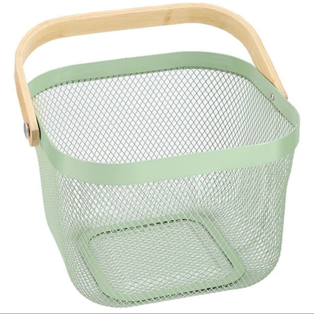A square metal mesh basket in a light sage green color, featuring a natural light wood handle and a matching green metal rim, shown on a plain white background.