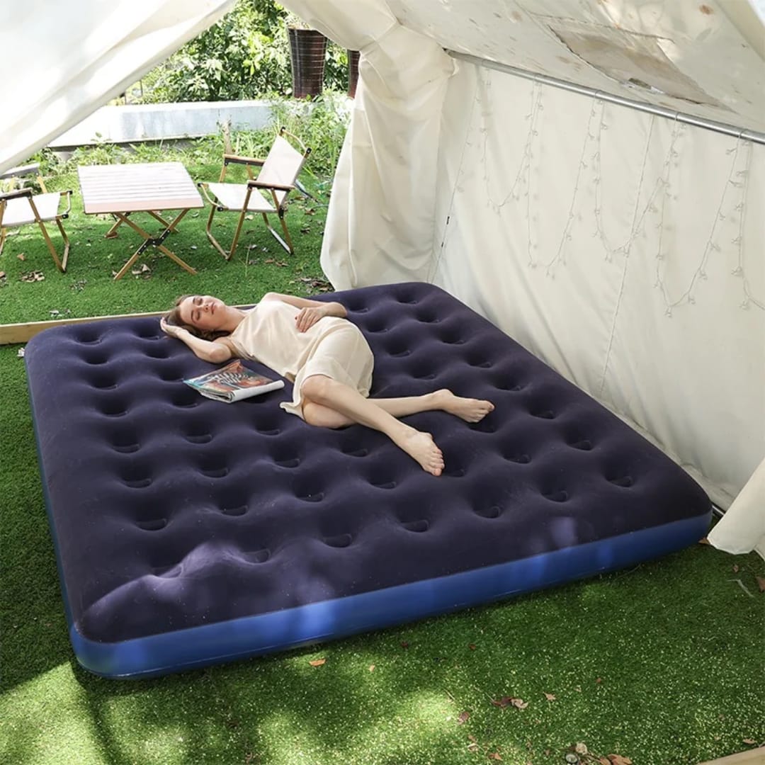 Person lying on an inflatable mattress outdoors next to a tent