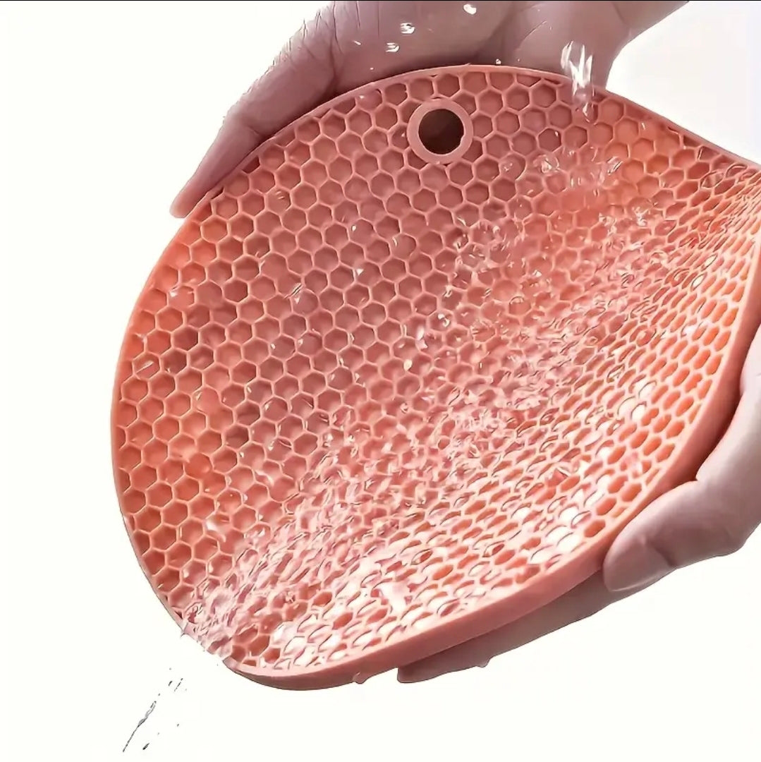 Pink silicone mat with honeycomb pattern held by a hand on a white background