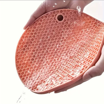 Pink silicone mat with honeycomb pattern held by a hand on a white background