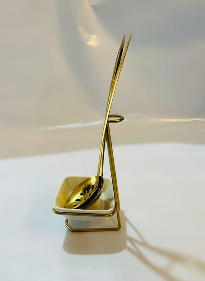 Gold-colored spoon and ladle set on a white surface with a soft shadow.