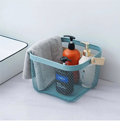 A teal blue wire mesh bathroom storage basket with a light wood handle, holding toiletries and a gray towel, set on a white bathroom counter.